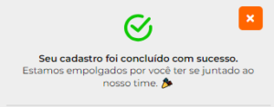 A imagem mostra uma pequena janela de notificação pop-up em um fundo cinza claro. Há um grande ícone de verificação verde à esquerda, indicando sucesso ou conclusão. O texto em português ao lado do ícone informa que o cadastro foi concluído com sucesso e expressa entusiasmo pela pessoa ter se juntado ao time. Um emoji de troféu é usado no final da mensagem para adicionar um toque amigável e congratulatório. No canto superior direito da janela pop-up, há um ícone “X” vermelho para fechar a notificação. 